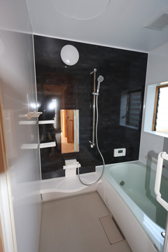 モダンなデザインのバスルーム。ブラックのアクセント壁がスタイリッシュであり、シャワーヘッドが実用的に配置されている。