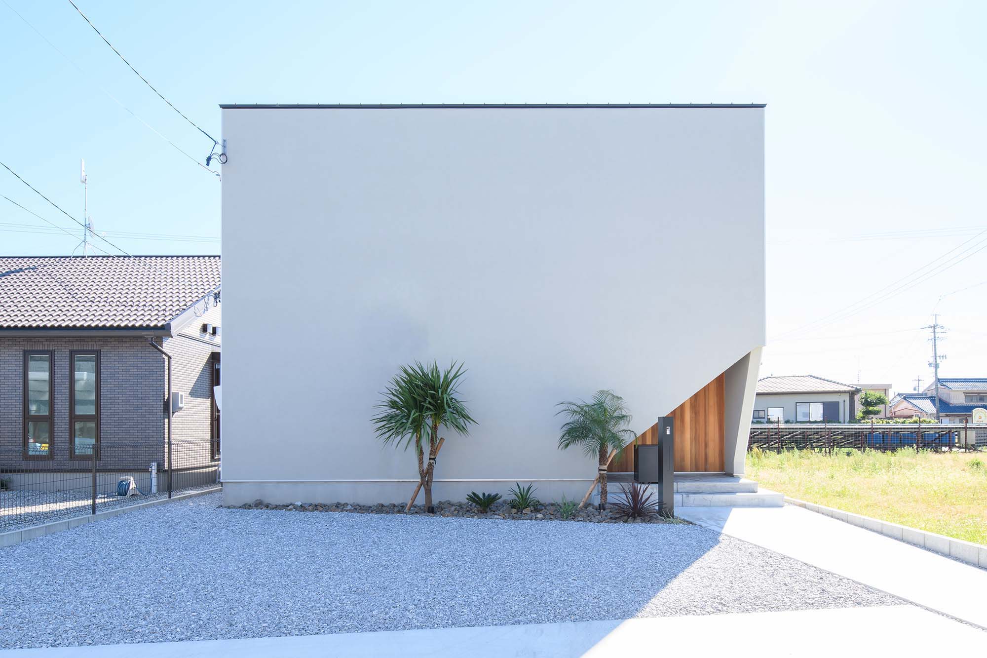 平屋建築ブルーハウス【デザイン住宅、間取り、建築家】道路側に面した、窓のないファサード。真っ白なボックスの一角を切り取り、玄関ポーチの板張りの外壁をのぞかせた斬新なデザインがインパクトを放つ