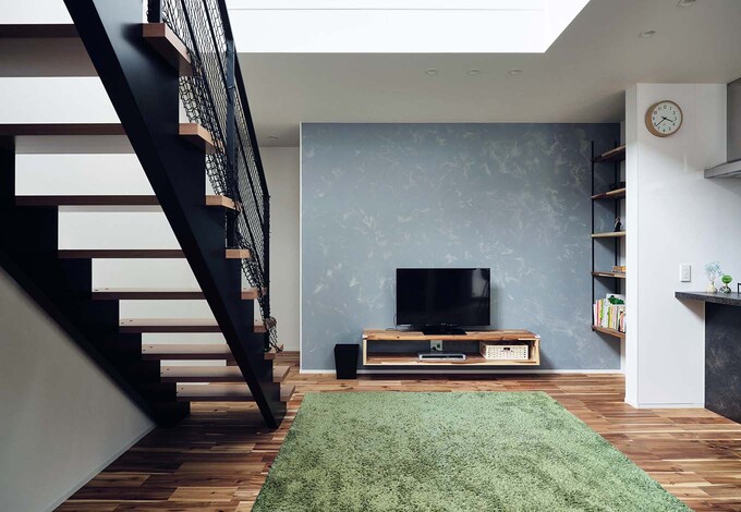 ニュアンスを醸すヘイムスペイントのアクセントウォールが、リビング空間をいっそうオシャレに引き立てる。テレビボードの横の収納棚を壁で隠し、雑多な印象にならないように配慮されている