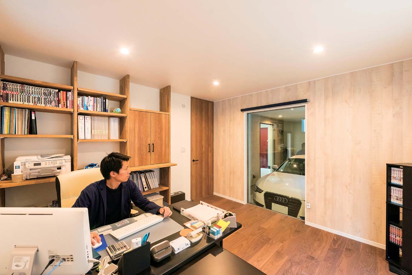 アトリエサクラ【デザイン住宅、間取り、ガレージ】事務所のフィックス窓からは、ガレージの愛車をいつでも眺められる。デスクまわりの書類棚は使いやすさを考慮して造作に