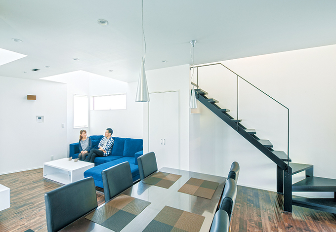 陰影が美しい白とダークブラウンの空間を黒い鉄骨階段が引き締める。木とアイアンの組み合わせが重厚感のあるダイニングテーブル「GEN」、ソフトな座り心地の椅子は「SIGUERRO」。ハコを造って終わりではなく家具までトータルにコーディネートするため、どちらも『納得』が開発したインテリア