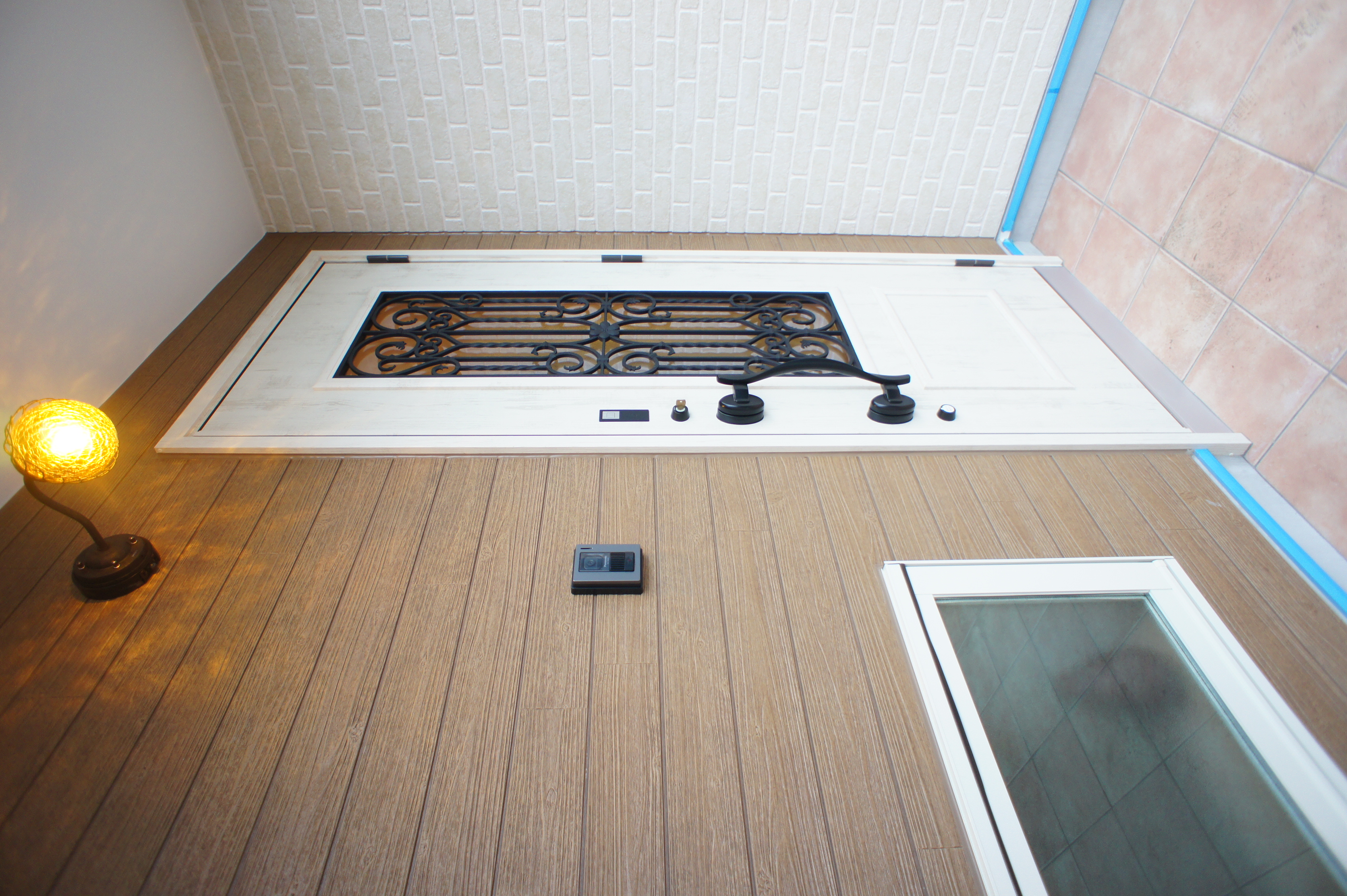 小野田産業～designers house project～｜アイアン格子が用いられたドアが印象的な玄関。落ち着いた色合いのタイルと木目調の壁が、温かみのある雰囲気を演出している。
