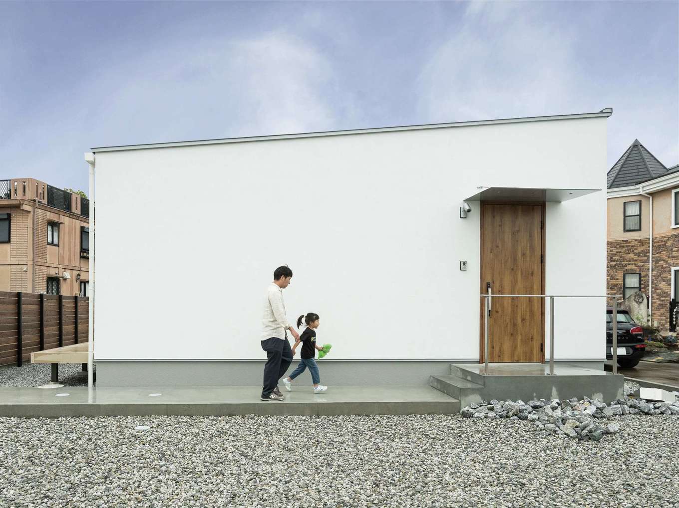 ひだまり工房【デザイン住宅、間取り、平屋】ライン、色、装飾、無駄を徹底的に省いた平屋建ての外観。白い塗り壁に木製の玄関ドアが映える。モルタルのアプローチもおしゃれ。エッジの効いた片流れの屋根には太陽光発電を搭載し、創エネ・省エネライフを実現した