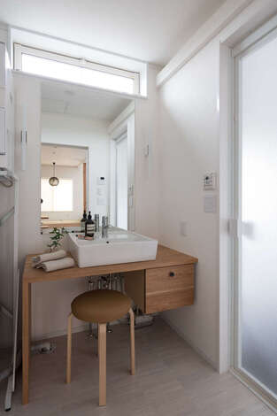 脱衣コーナーに設けた造作の木製洗面台。引き出しと脚部分のアシメトリーな造りがデザインへのこだわりを感じさせる。スツールを置けるようにカウンターの下をオープンにしてあるため、座ってゆっくりメイクやスキンケアができる