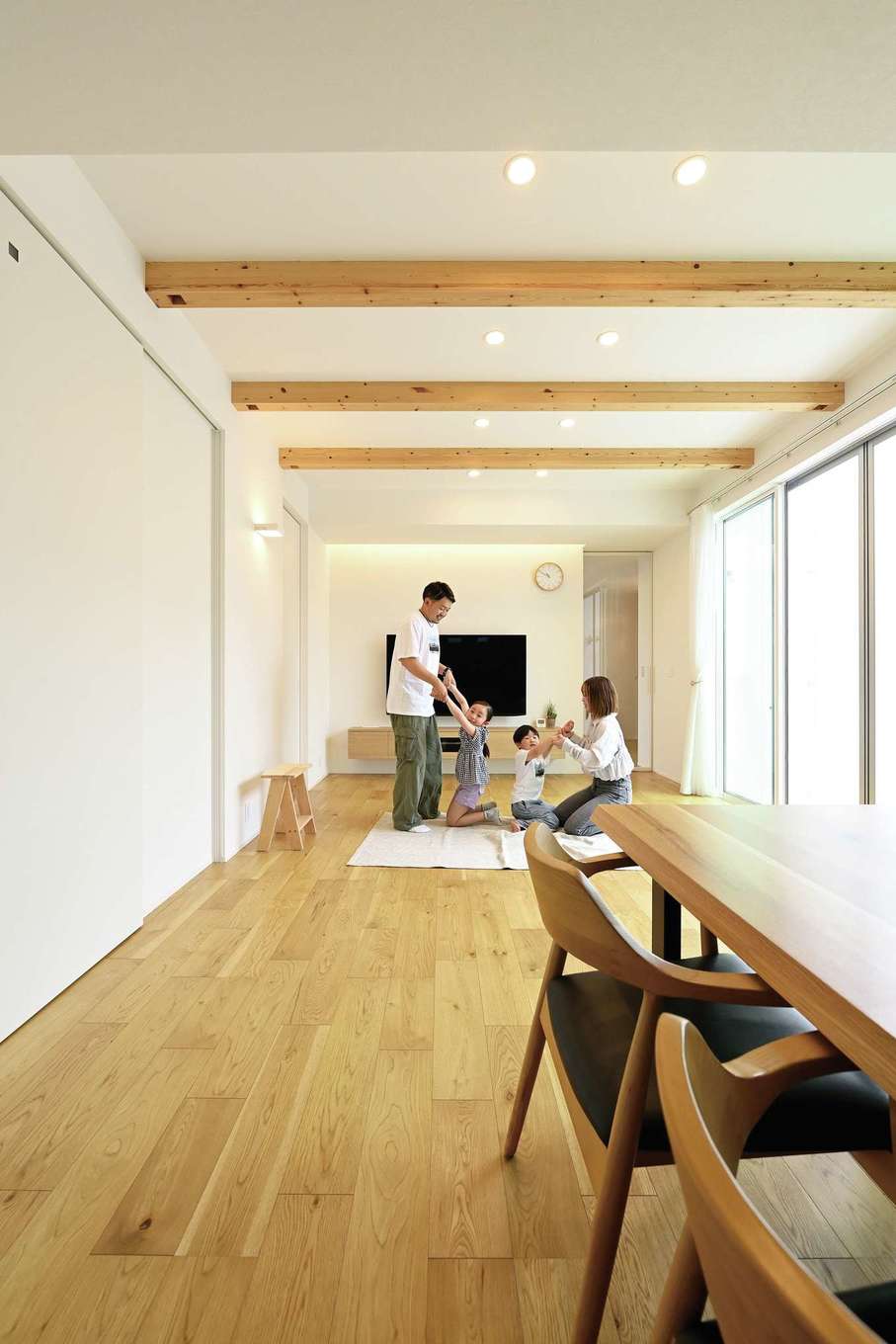 REIWA HOUSE（令和ハウス）【デザイン住宅、省エネ、間取り】東西に長い敷地を活かした21畳のLDK。リビングの大開口から差し込む光が白い壁に反射して明るい居住空間を実現した。リビングとダイニングキッチンの天井高を変え、現しの意匠梁を設けたことで空間がより広く感じられる