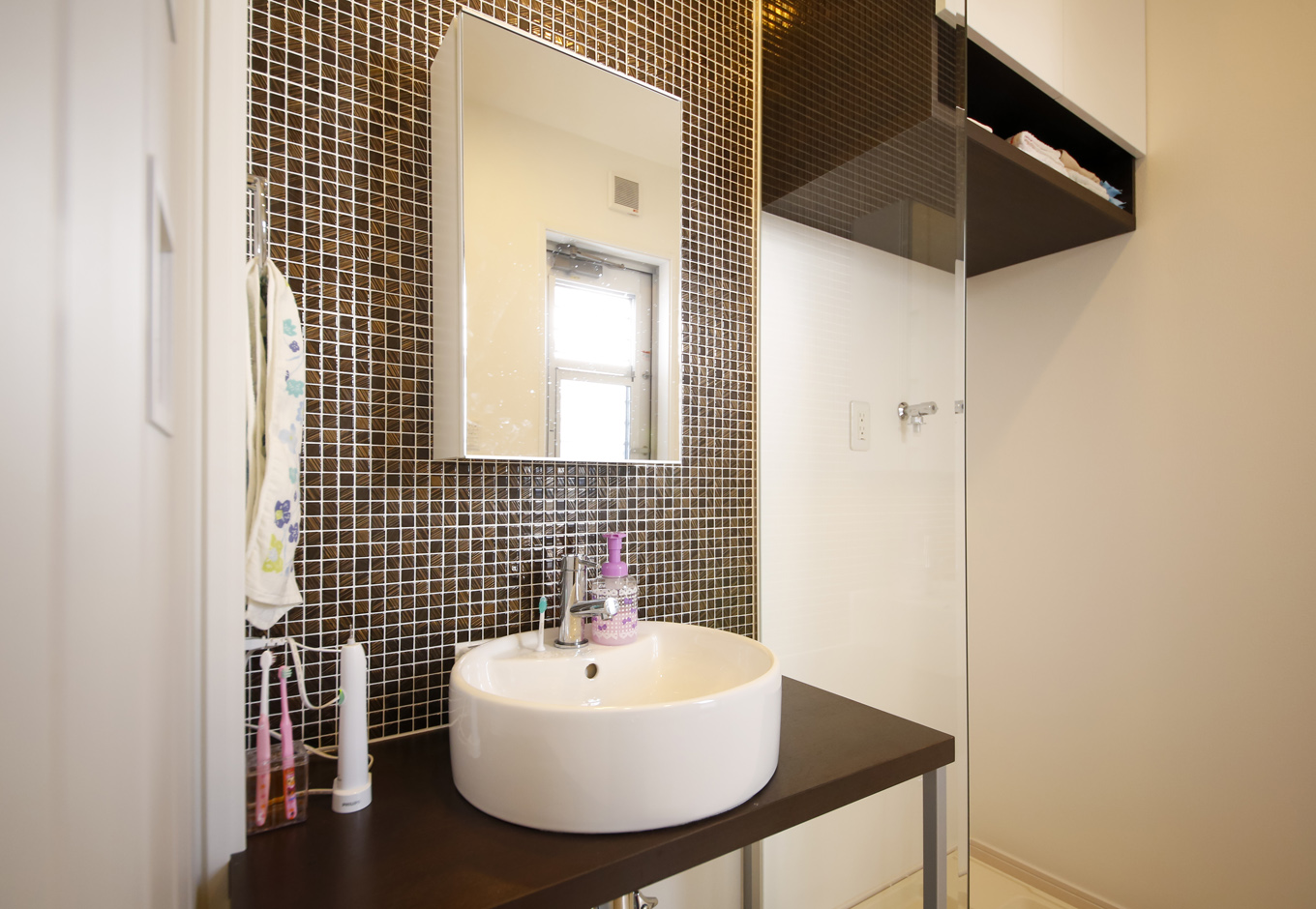 丸昇彦坂建設【デザイン住宅、間取り、インテリア】洗面スペースもモダンなデザインに仕上げた。モザイクタイルを張り付けた壁が印象的だ