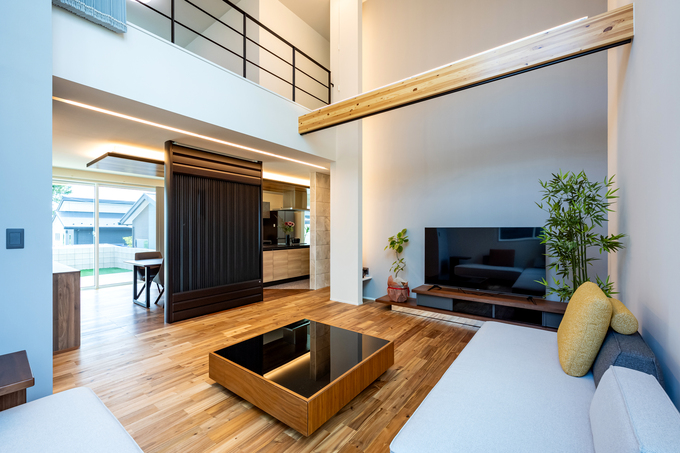 開放的な吹き抜けが特徴のLDK。リビングには大画面テレビが配置され、家族がくつろげる空間を演出している。明るい自然光が差し込み、温かみのある床材が雰囲気を引き立てている。