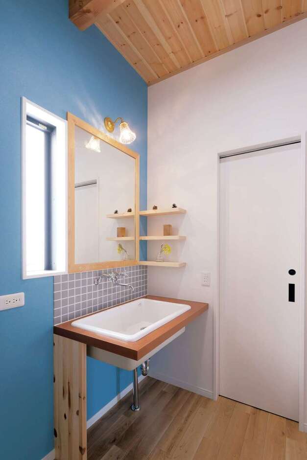 ブルーのアクセントクロスにシンプルなデザインのオリジナル洗面台が映える。鏡も洗面台に合わせて造作したもの