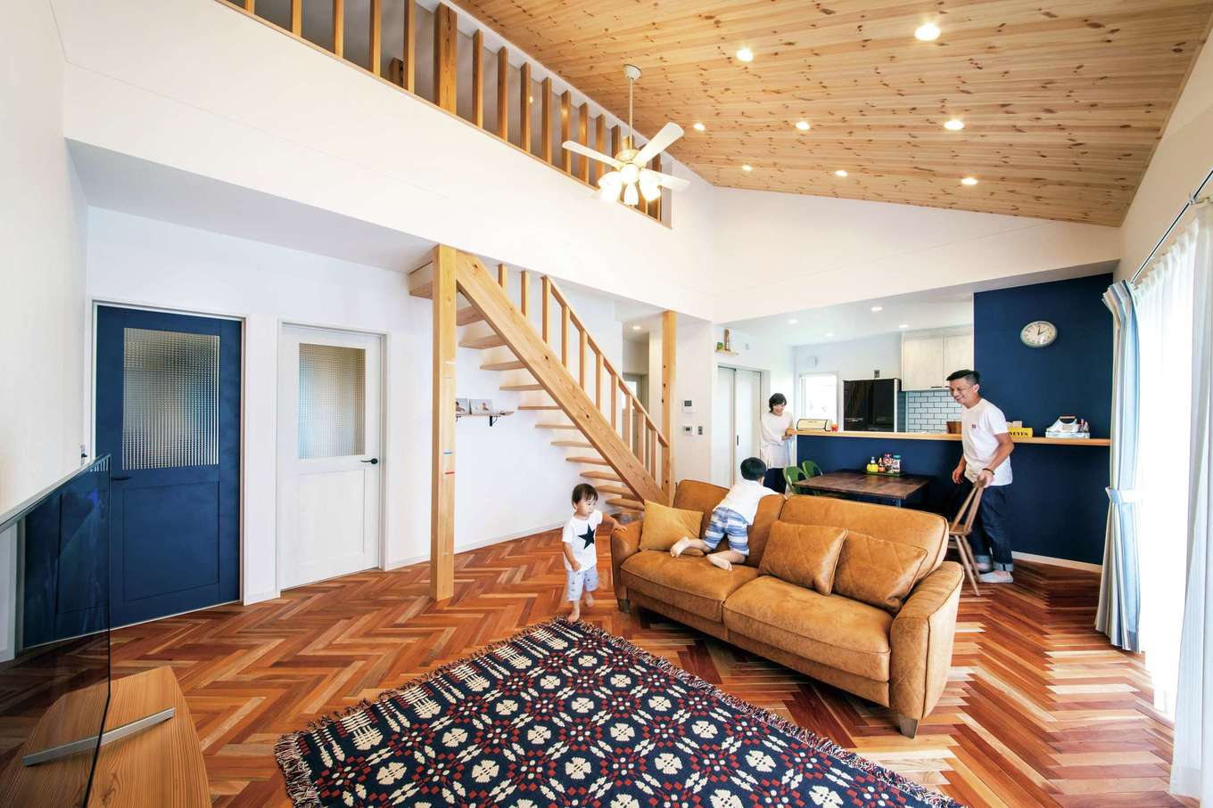 水田建設【デザイン住宅、省エネ、平屋】ヘリンボーンの無垢の床が広がる本格カリフォルニアテイストのLDK。勾配天井が開放感をもたらし、ネイビーブルーのドアやキッチンが広い空間を引き締めている