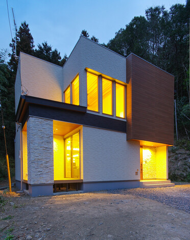 モダンなデザインを持つ2階建て住宅の外観。大きな窓から温かい灯りが漏れ、夜の風景に独特の魅力を添えている。