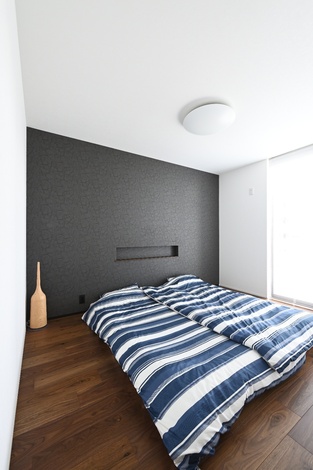 落ち着いた色合いの寝室である。シンプルなベッドとダークカラーのアクセントウォールが印象的で、リラックスできる空間を提供する。