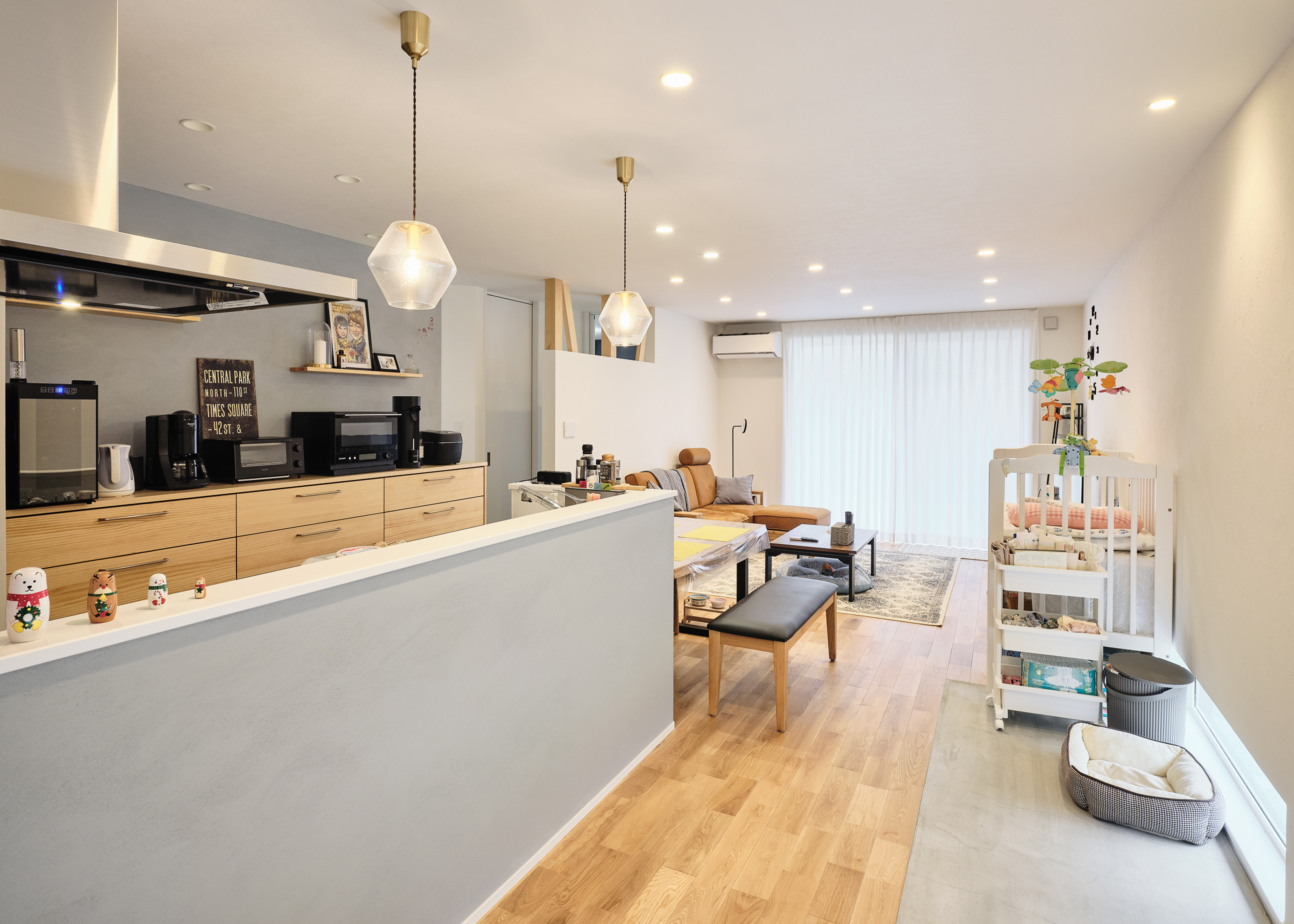 平屋建築ブルーハウス【ペット、建築家、平屋】玄関の土間はLDKまで続き、リビングとの境目に段差のないユニバーサルデザインを採用。LDKの土間部分は愛犬の居場所としても活躍する。対面キッチンの腰壁とキッチンの背面の壁は塗り壁で仕上げ、本物素材の質感が室内の雰囲気を引き立てている