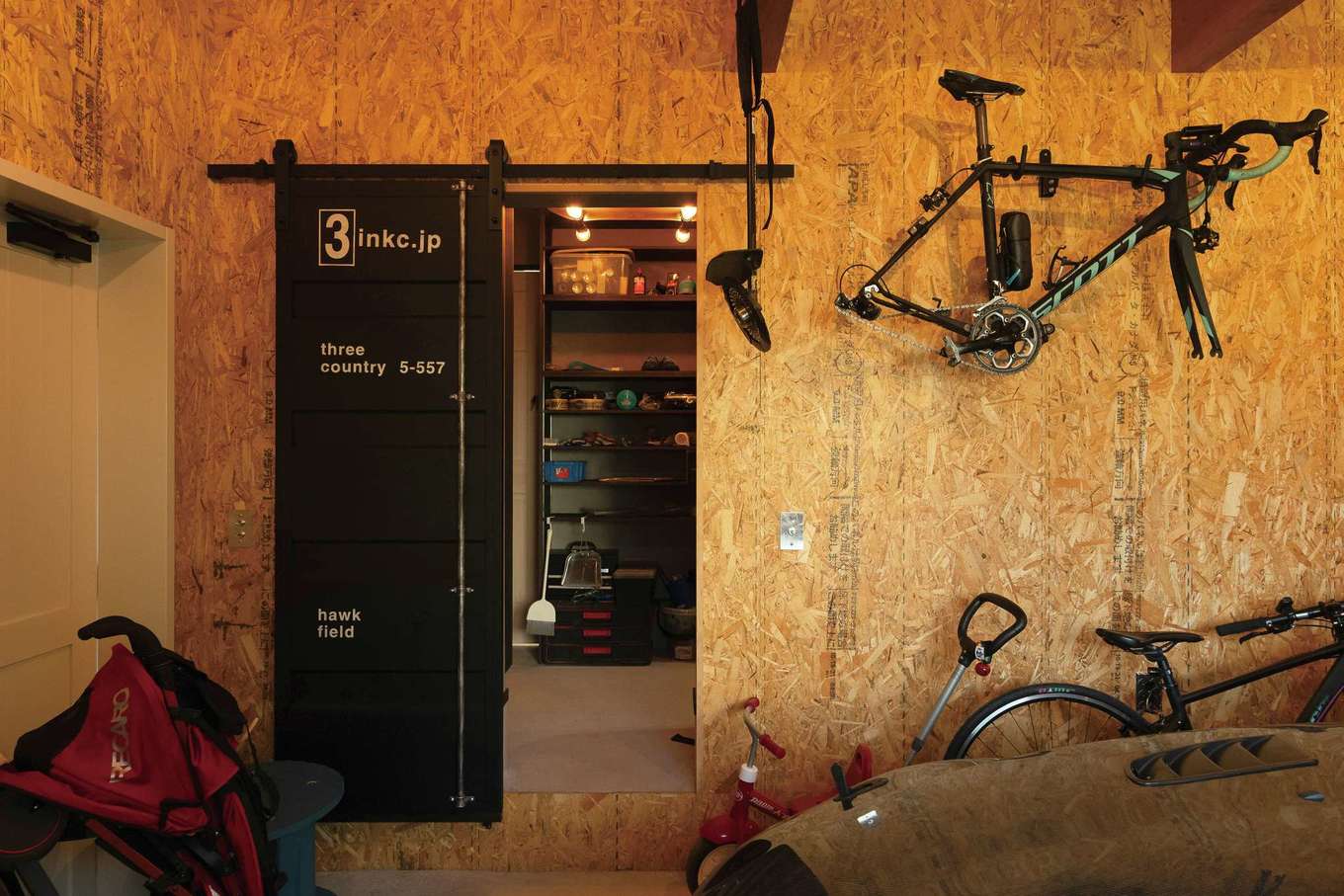 富士ホームズデザイン【輸入住宅、趣味、ガレージ】室内からもアクセス可能なガレージ。木質ボードとファクトリー感のある引き戸により、ワイルドな空間に。アウトドアグッズやロードバイクに加え、現在はお父さまの愛車を保管する