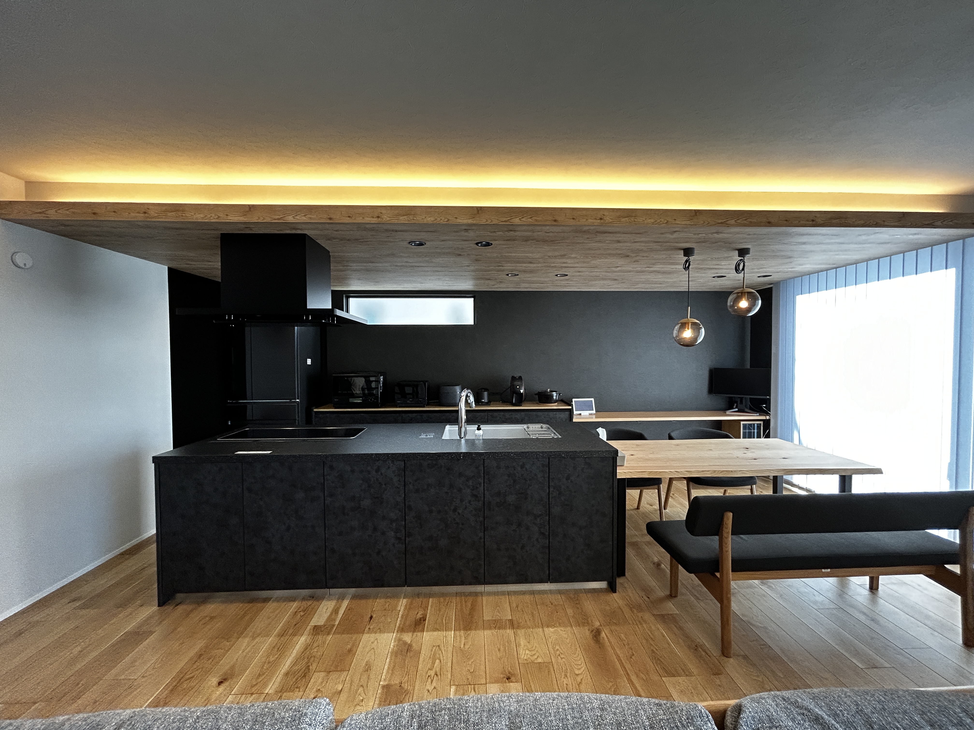 パナソニックホームズ中部第一支社 愛知第一支店・愛知第二支店｜モダンなデザインのLDK。広々とした空間に、ダークなトーンのキッチンと家具が調和している。大きな窓から自然光が差し込み、明るく開放的な雰囲気が魅力。