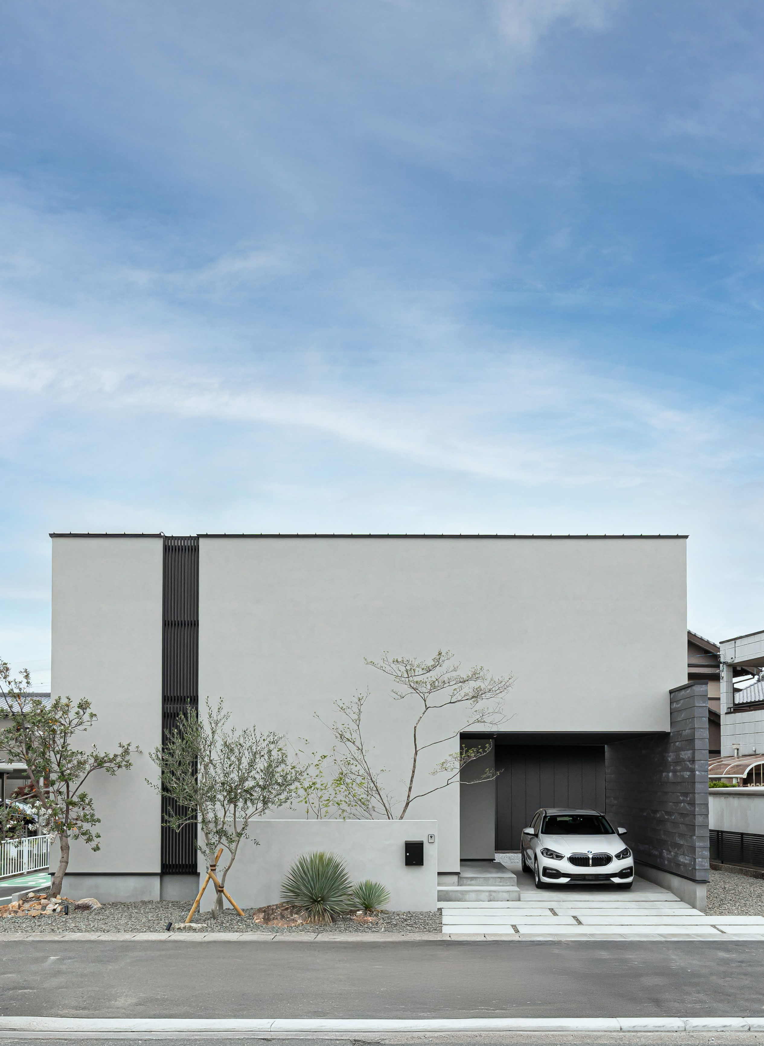 ARRCH アーチ【浜松市中央区笠井町1018-3・モデルハウス】住宅街の52坪の敷地に立つインナーガレージ付きの二階建て。ガレージの奥や建物の横にも駐車場スペースを確保し、合計3台駐車可能。塗り壁の外壁をベースに、「SOLIDO」の鎧張り風の壁や、木目調のコートラインをプラスして個性を演出した