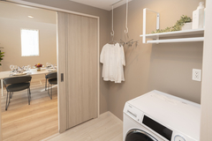 機能的なランドリールームには洗濯機が設置されており、近くにはディナーを楽しむダイニングも見える。快適な家事動線を実現。