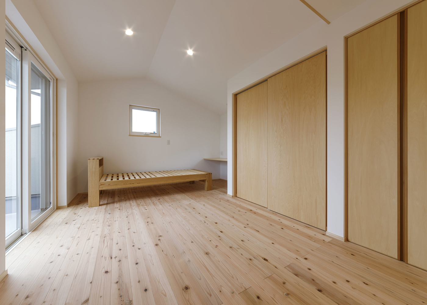 灯建築舎【デザイン住宅、和風、自然素材】2階に配されたご主人の寝室。高さを抑制した勾配天井が、気分を落ち着かせてくれる。奥には仕事用のカウンターを設置。右手の収納に加え、左側手前には廊下側からも出入り可能なウォークインクローゼットが用意されている