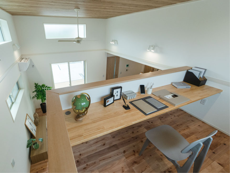 ヘスタホーム｜木の天井が温かみを添える、明るい中二階スペース。高すぎ天井を活用した壁沿いの長いカウンターデスクでテレワークや趣味を楽しめます。リビングを見下ろせる設計で、家族とのつながりも大切に。