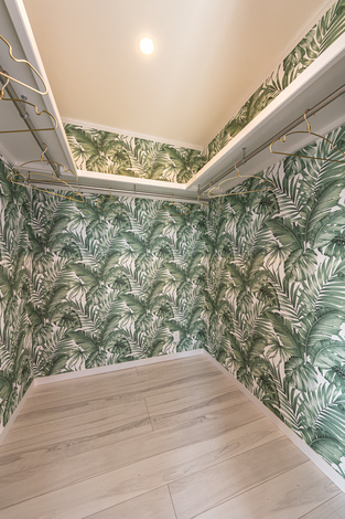 葉っぱの壁紙が印象的なウォークインクローゼット。広々とした空間と複数のハンガーレールがあり、効率的に衣類を整理できる。