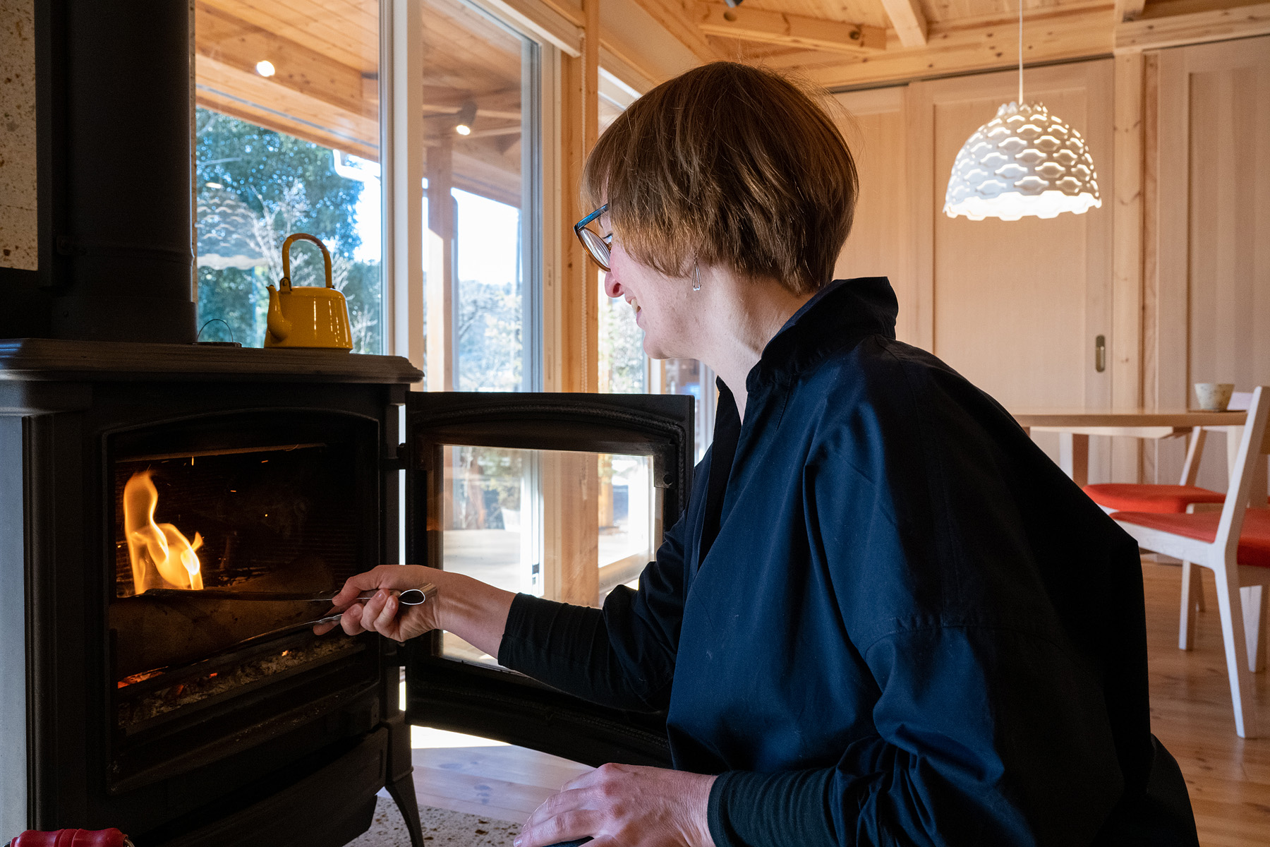 ネクストハウスデザイン｜薪ストーブの前で火を楽しみながらリラックスできるリビング空間。大きな窓が外の景色を取り込み、自然を身近に感じる空間づくりに貢献している。