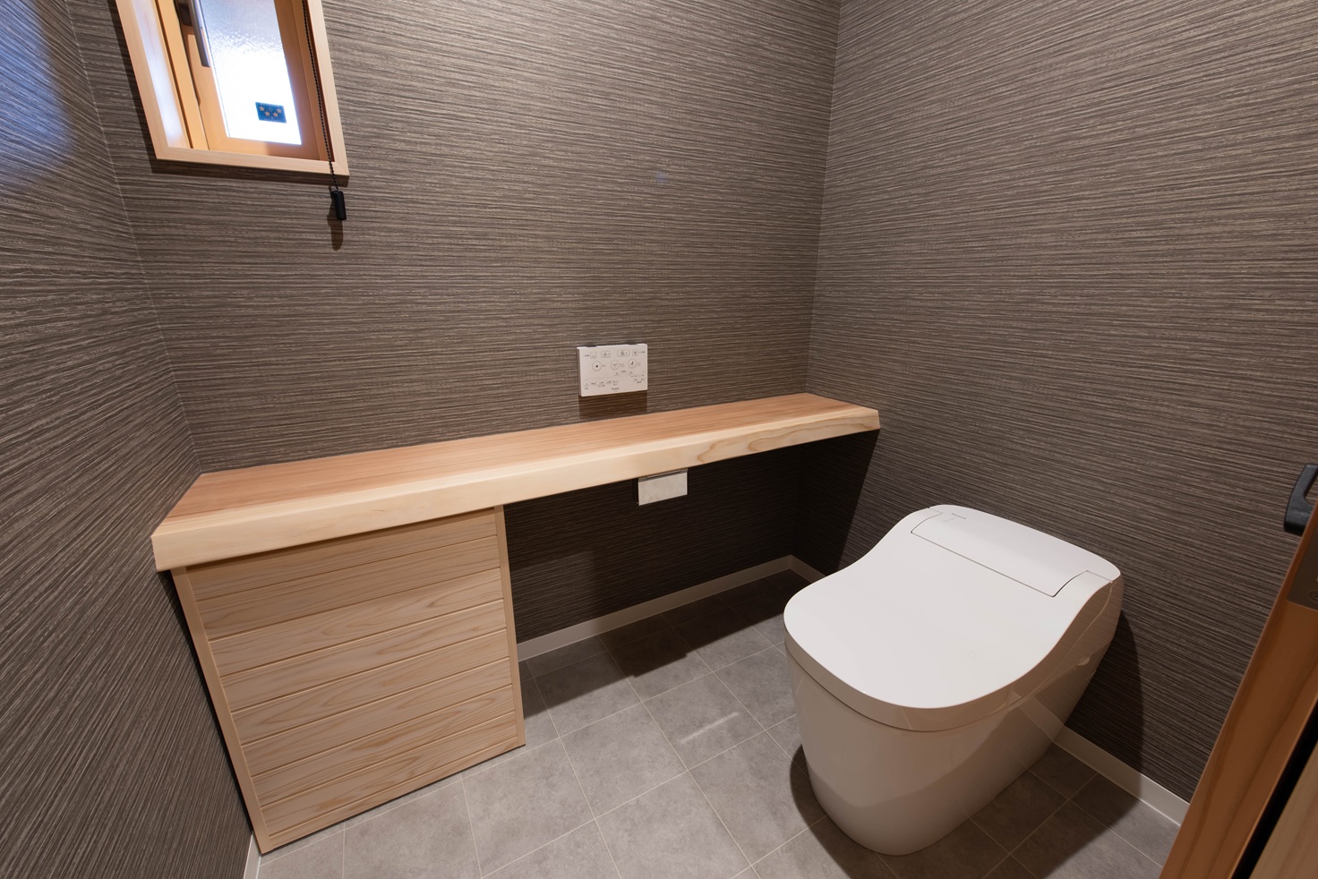 カネタケ竹内建築｜シンプルで洗練されたトイレ空間。ウッド調カウンターとグレーの壁紙が落ち着いた雰囲気をつくり出している。