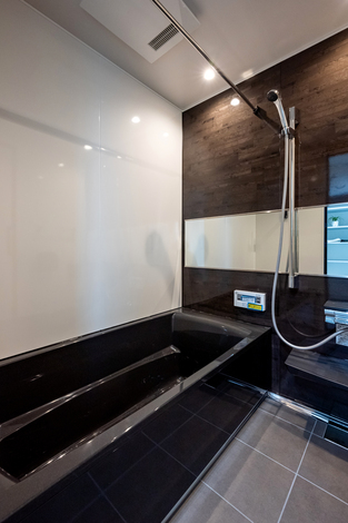 モダンなデザインのバスルーム。ダークトーンのタイルと光沢のあるパネルが高級感を演出し、リラックスできる空間となっている。