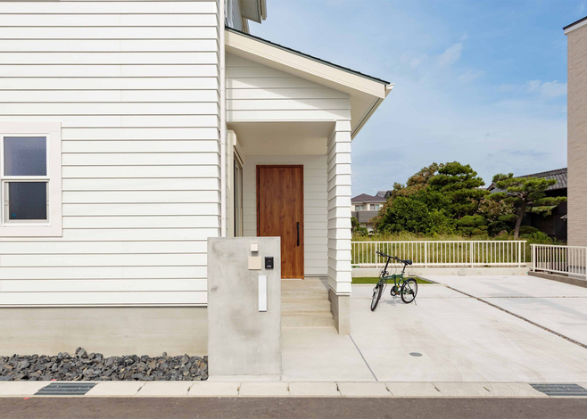 白いラップサイディングに木の扉が映える