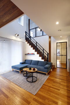 木製の床が美しい内装に、ブルーのソファがアクセントとして配置されたLDK。開放的な空間とスタイリッシュな階段が調和している。