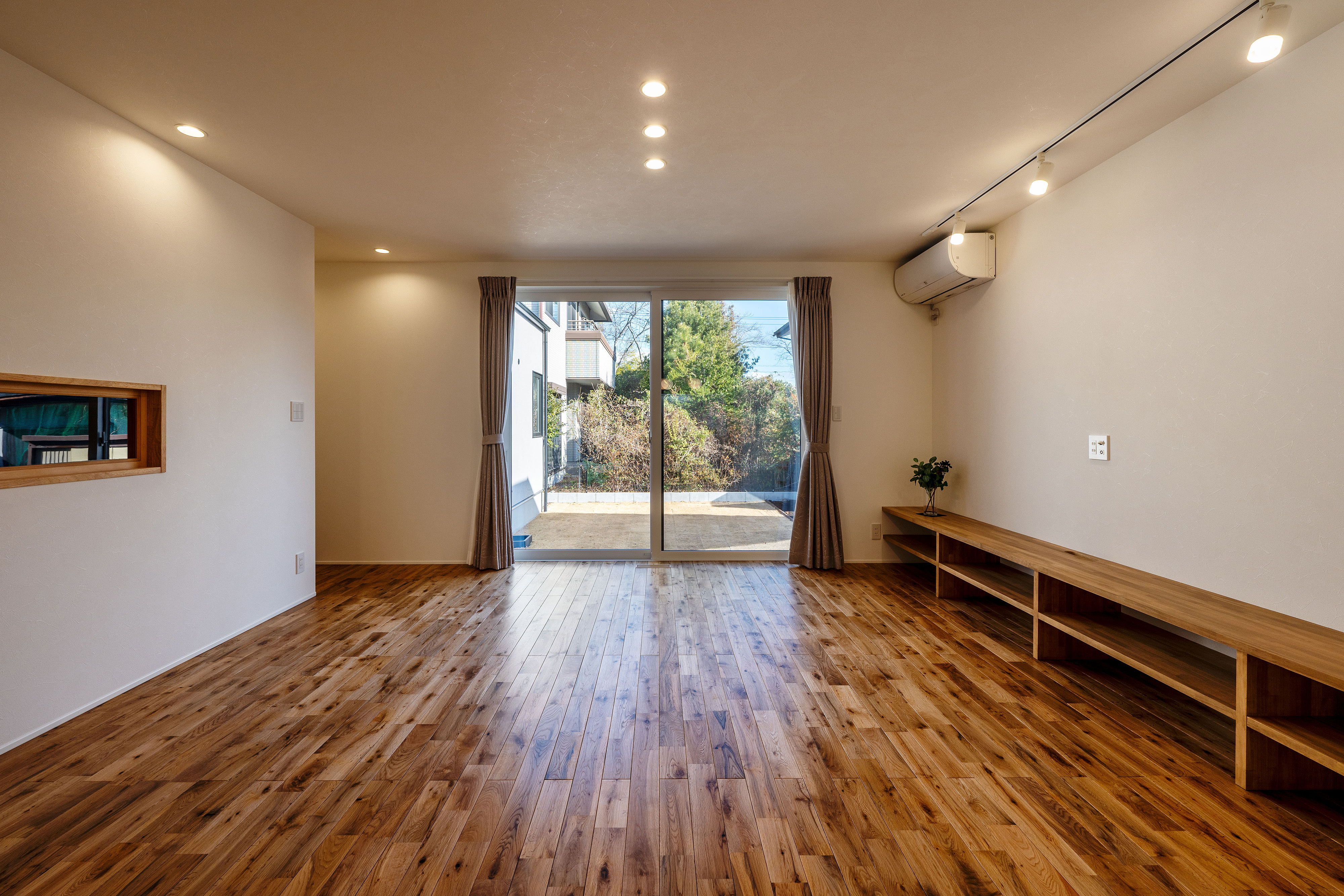 ハウスプラン（R＋house沼津・富士）【間取り、建築家、平屋】床には無垢のオークが敷かれ、ほっとくつろげる雰囲気。造作のTVボードが統一感をもたらしている。ひとつながりの庭からは広さと明るさが届く