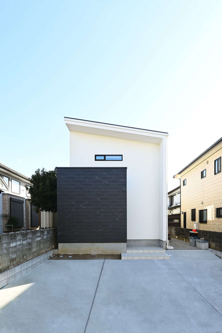 トーリンホーム【デザイン住宅、子育て、間取り】片流れの屋根と白×黒のコンビネーションがクールな外観。道路側からの視線を遮るために玄関ポーチを黒い塀で隠している。黒い塀はコンクリート系の新素材「ソリド」を採用。自然のムラによる個性的な風合いとざらりとした素材感が外観の意匠性を高めている