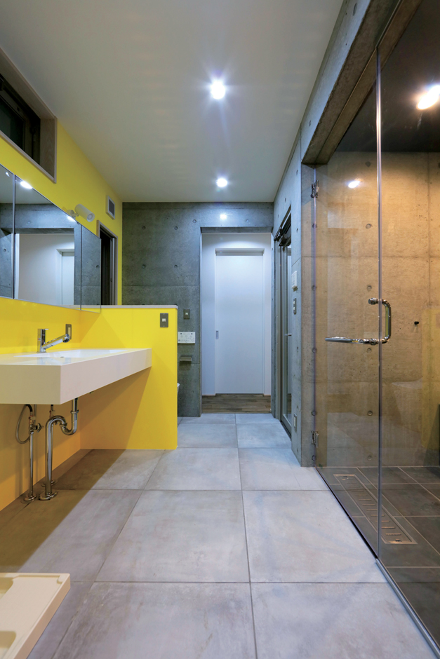BAUM HOME（岩崎工務店）【デザイン住宅、平屋、鉄骨鉄筋コンクリート構造】キッチンからも寝室からもつながるサニタリー。鮮やかなイエローが差し色に。ガラス張りの浴室は造作で、中庭に面している
