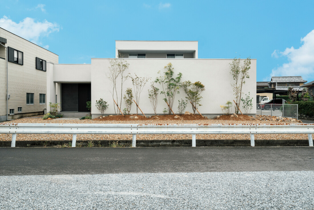 チェックハウス｜植栽に囲まれたモダンな住宅の正面。シンプルで洗練されたデザインが、地域の風景に溶け込んでいる。
