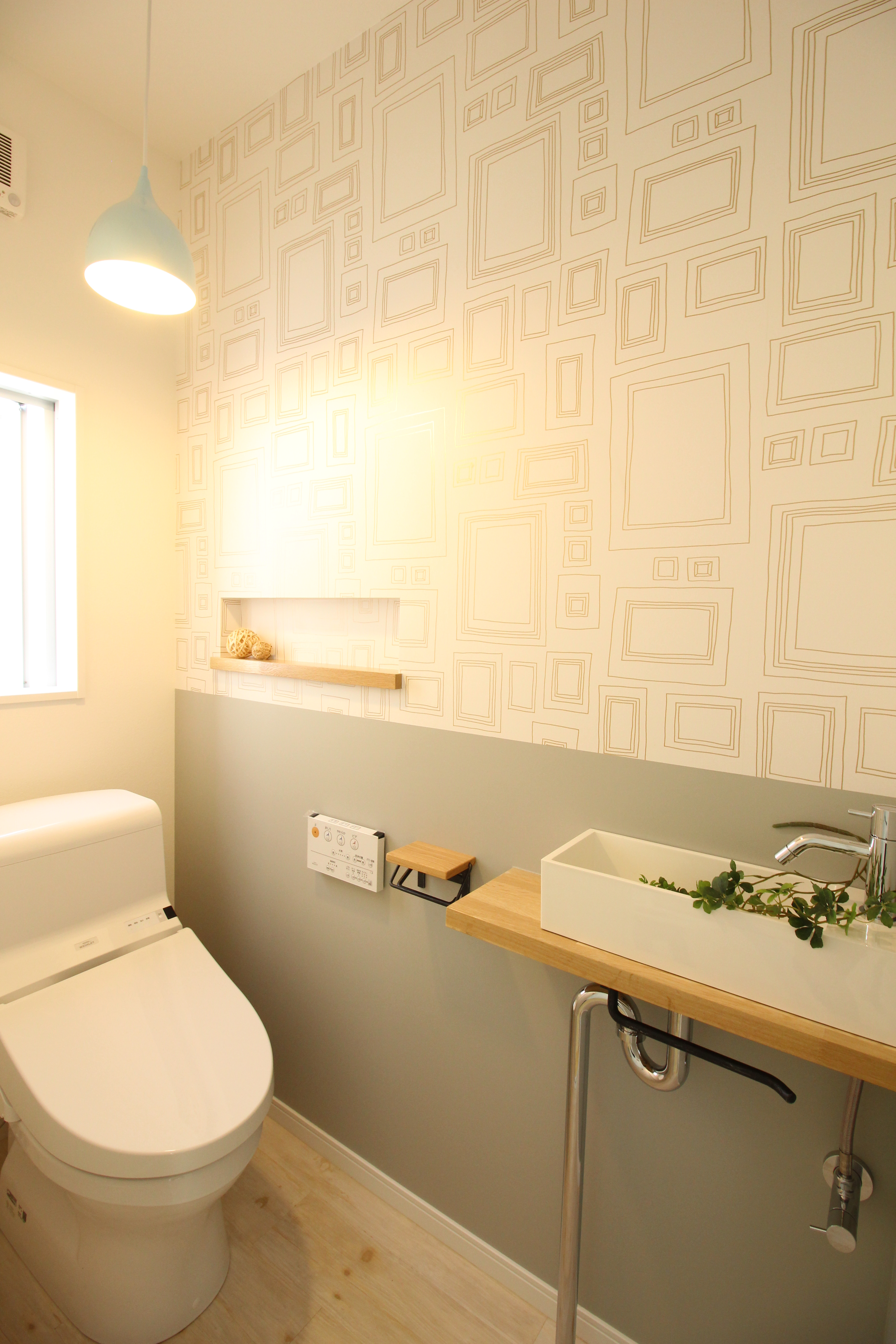 小野田産業～designers house project～｜明るいペンダントライトが照らすトイレ空間。壁のデザインがスタイリッシュで、ナチュラルなウッドのカウンターが落ち着いた印象を与える。