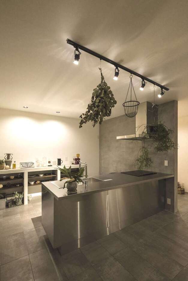 存在感のあるステンレスキッチンを主役に。サイドの壁はモルタル塗装で、床の質感とコーディネート。背面の収納棚もフレームはモルタルづくり、棚板は無垢材を用いた