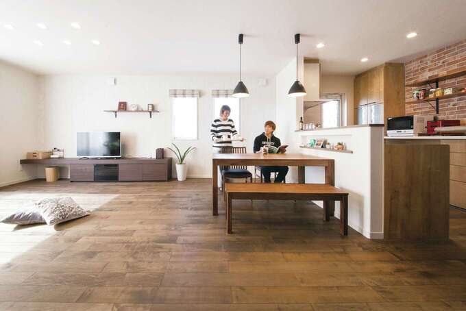 無垢材の床にレンガ調タイル、デザイン照明が映えるLDK。ここでくつろぐのが夫婦の楽しみで、ご主人の趣味の筋トレを一緒に行うことも