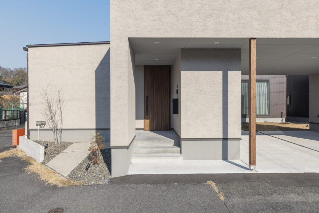 チェックハウス｜シンプルでモダンなデザインの建物外観。広い車寄せと玄関へのアプローチが、使いやすさと美しさを提供している。