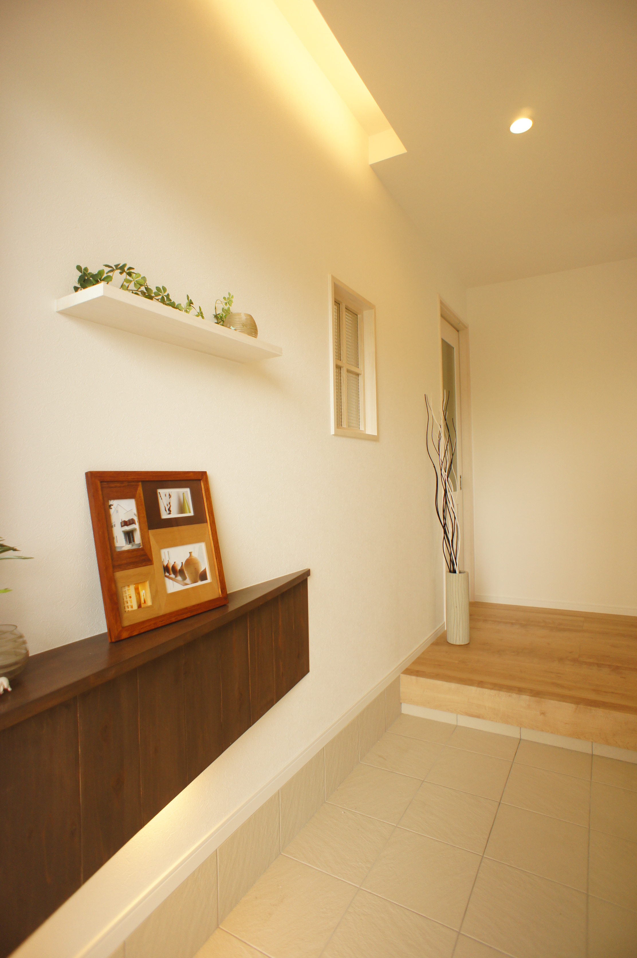 小野田産業～designers house project～｜温かみのある照明が設置された玄関ホール。壁の飾り棚には写真とグリーンを配置し、訪れる人を迎える空間に仕上がっている。