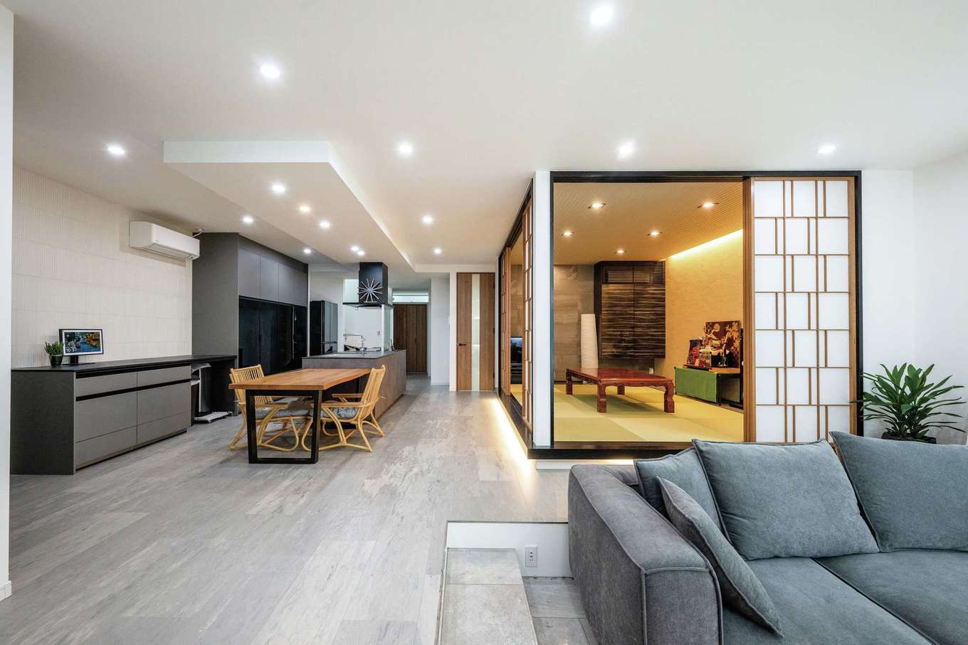 irohaco（アヴァンス）【デザイン住宅、高級住宅、間取り】和室と合わせると30畳を超える子世帯のLDK。インテリアをグレージュなトーンで統一し、リビングをフロアダウンしたことで空間に変化がついた。和室は小上がりに間接照明を採用し、障子のデザインにもこだわった