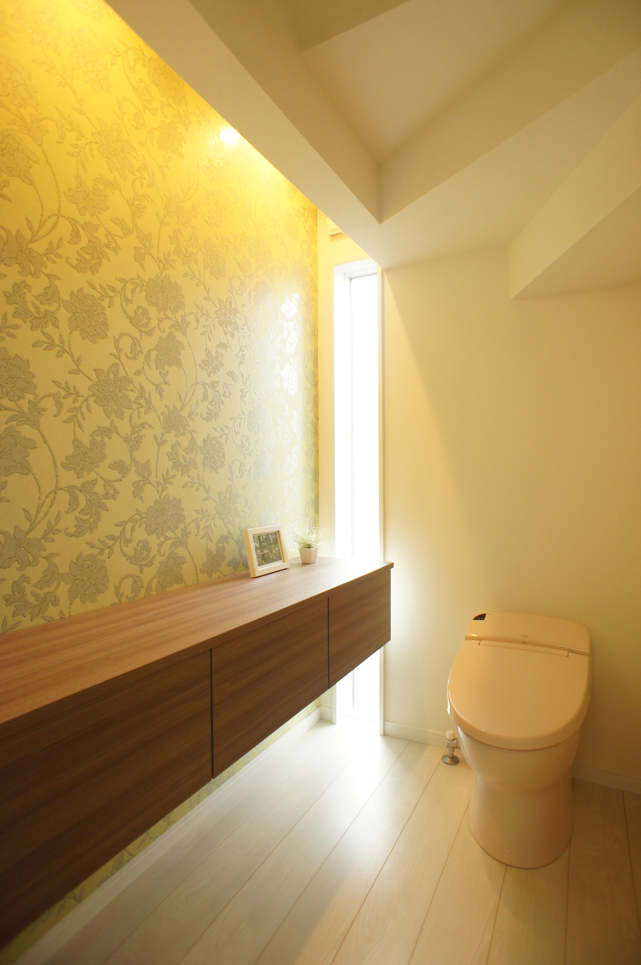 小野田産業～designers house project～｜落ち着いた雰囲気のトイレ。木目調の収納とアクセントクロスが空間に温かみを与え、心地よいひとときを提供するデザインである。