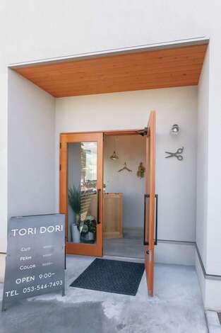 美容サロンのエントランス。板張りの軒や木の扉が塗り壁に映える。地域の人々に何のお店かわかってもらえるように、壁にスチール製のハサミのオブジェを飾った