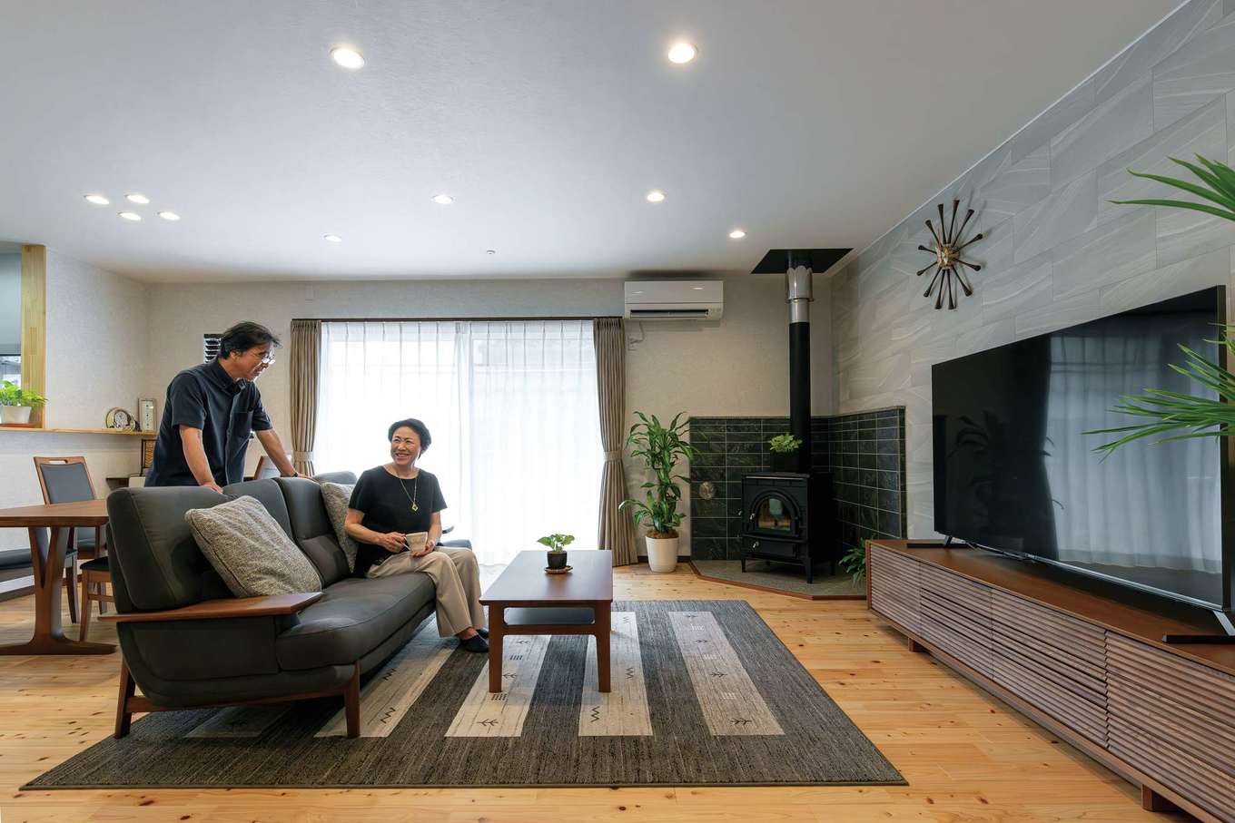 片山建設【デザイン住宅、夫婦で暮らす、平屋】同社ならではの頑強な構造により、優れた耐震性と開放感を両立したLDKには、さらりとした質感のヒノキが家全体に敷き詰められた。薪ストーブ部分の床と壁には御影石。同じ形の石が張られることが多いが、上にいくほど幅を狭くするなど細かな要望が叶えられた