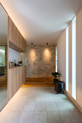 高級感のある玄関ホール。木目調の収納と石材を使った壁がアクセントとなり、モダンな印象を与える。自然光が差し込む明るい空間。