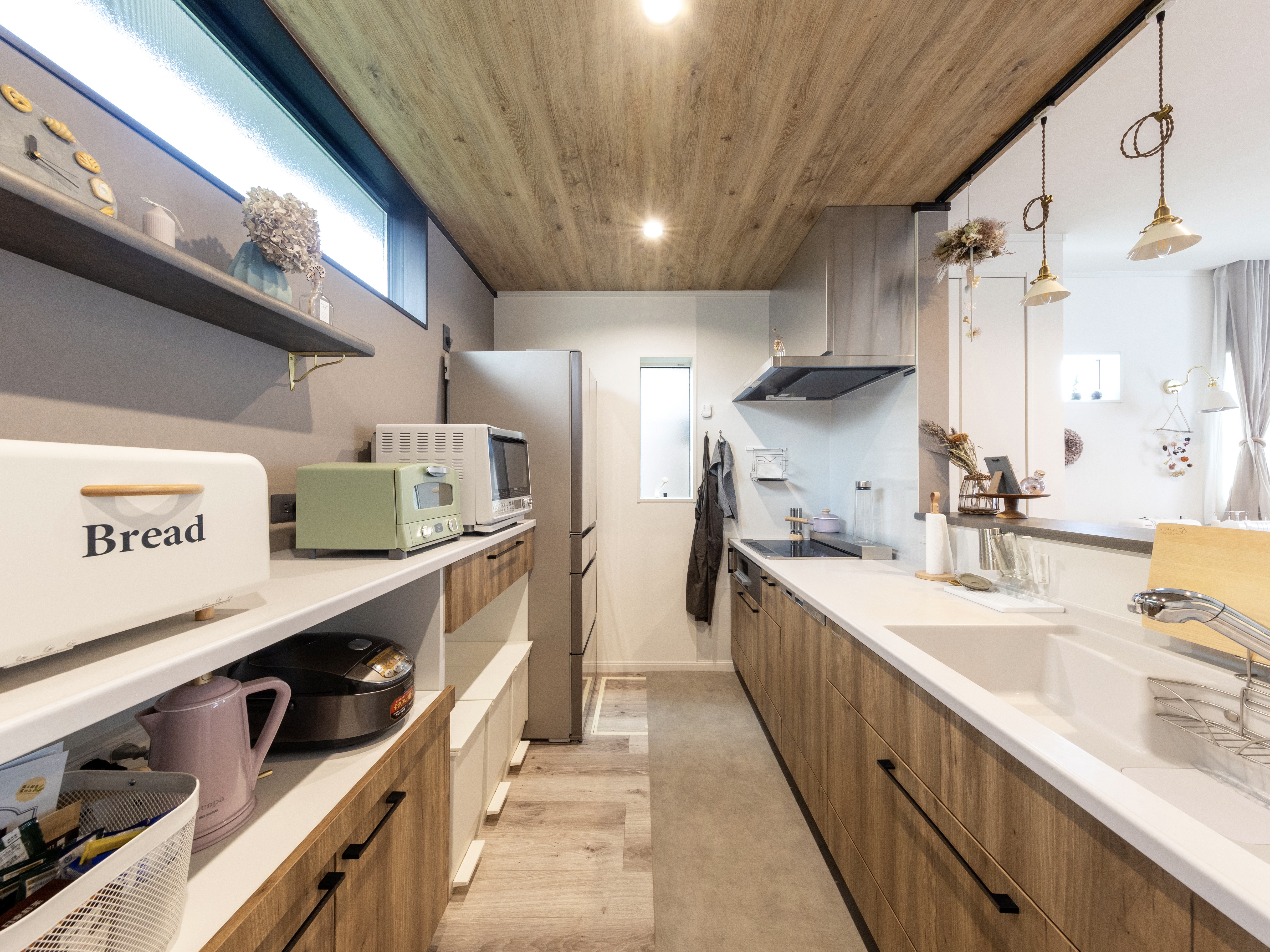 エスホーム｜木目調の天井とキャビネットが温かみを演出するキッチン。ゆったりとしたスペースで料理がしやすく、収納も充実している。