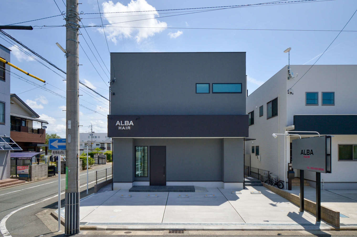 スズイチ【夫婦で暮らす、屋上バルコニー】トレンドカラーのグレーの塗り壁が落ち着きを感じさせる外観。1階が美容室「ALBA HAIR」、2階が住居になっている