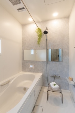 シンプルでモダンなデザインのバスルーム。明るい白を基調とし、壁面にはアクセントとしてグレーのタイルが配置されて落ち着いた雰囲気を演出している。