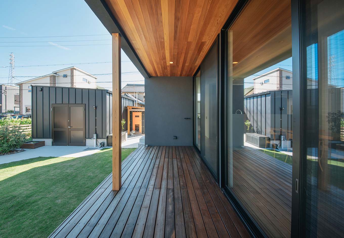 平屋建築ブルーハウス【デザイン住宅、建築家、平屋】耐久性に優れたイタウバの広いウッドデッキが、庭をいっそう身近にする。レッドシダー張りの軒天が、シックな外観にほどよい明るさと重厚感をプラス。庭の一角には、外観と色を統一したバイクガレージを置いた