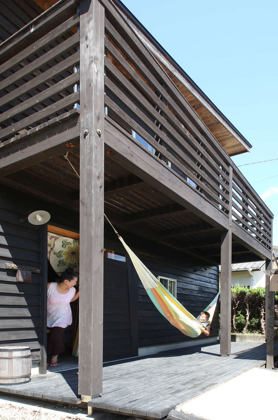 有吉住宅【子育て、趣味、自然素材】カバードポーチも子どもたちにとっては貴重な遊び場。木製の玄関ドアはオーダー。流木のような手すりは設計士の纐纈さんが探してきて加工した