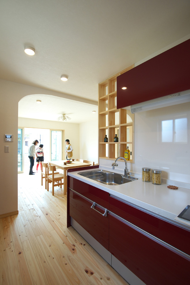 ワイズホーム｜奥さまの希望で採用した赤いキッチンが、自然素材の空間によく映える。キッチン横の飾り棚はワイズホームが造作した