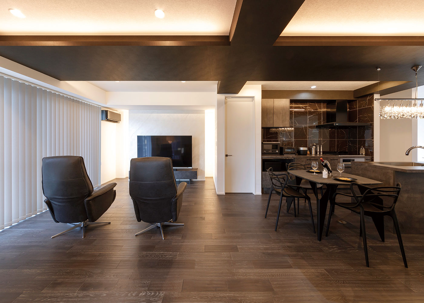 nattoku住宅｜キッチンとリビングを繋ぐ下がり天井。立体的な造形で間接照明の陰影が映える。家族全員が座れるソファではなくリクライニングチェアを採用し、ゆったりと映画鑑賞を楽しめるようにした。リビングのTVウォール裏にはリビングから隠すように収納スペースを設置。光をアクセントウォールにするというデザインを取り入れた