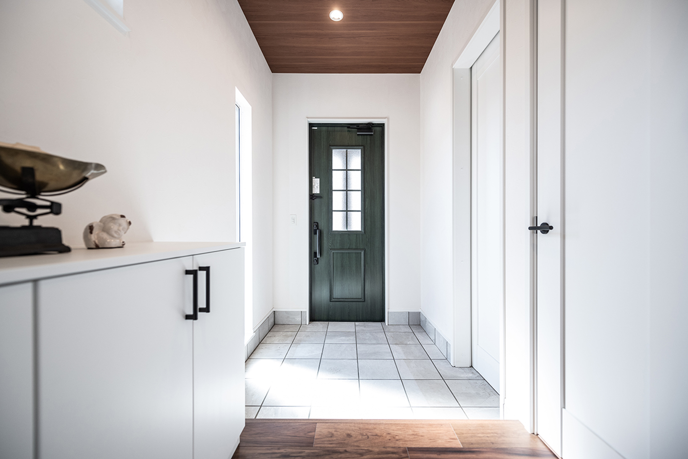 OWN RESORT HOME（オウンリゾートホーム）【デザイン住宅、趣味、インテリア】オリーブドラブの玄関ドアが映える真っ白なエントランス。マットな白い建具もキッチンやトイレと同じPanasonic製で、実寸よりも広く感じられる。水回り、リビングそれぞれの方向にアクセスできる2WAY動線を確保した